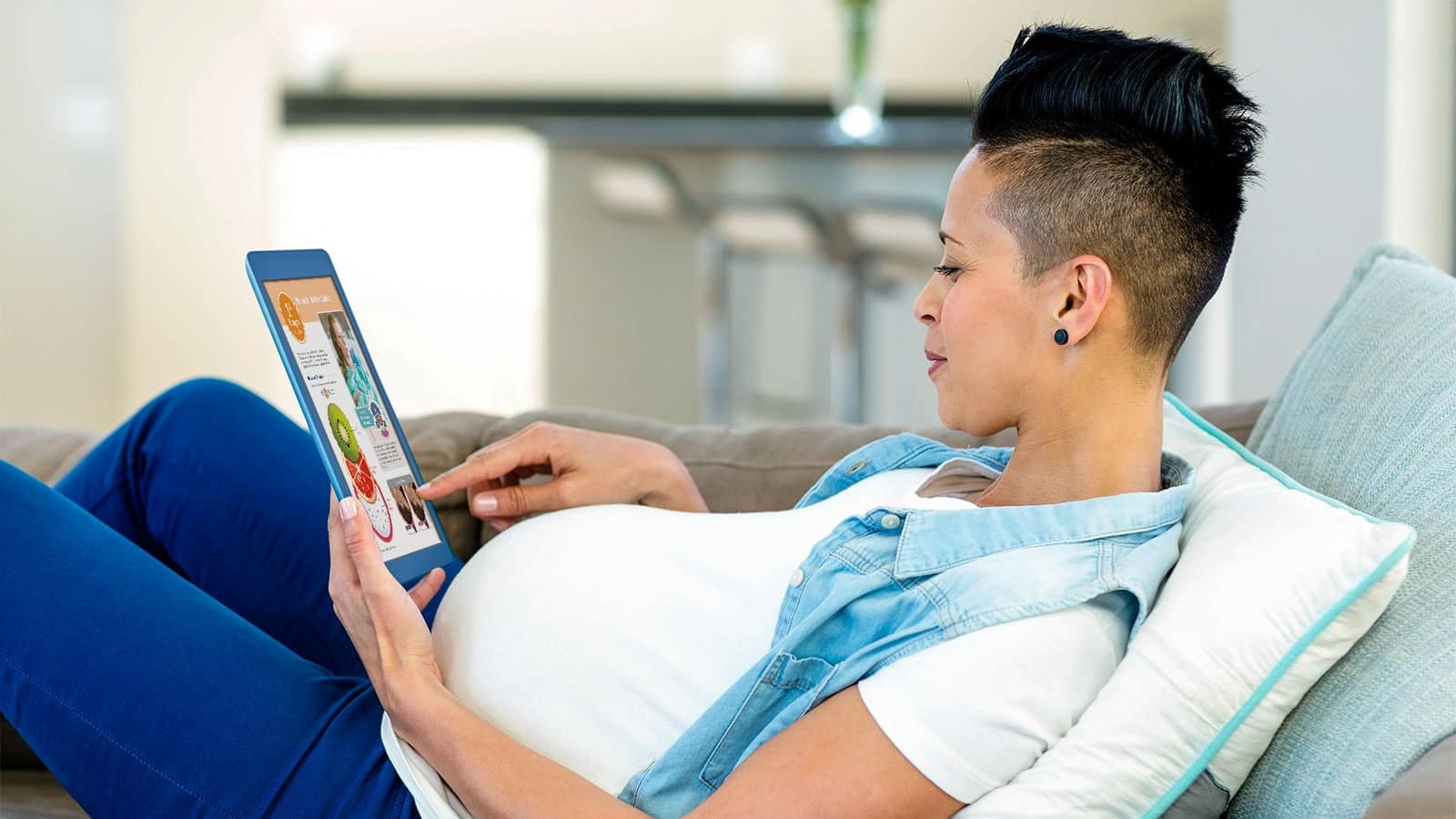 Expectant parent relaxing on the sofa while reading an ebook on a tablet.